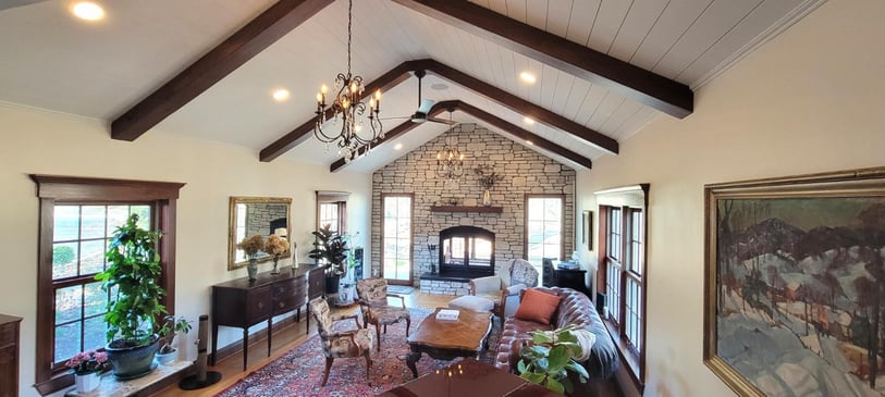 Dayton, OH custom home living space by Reliable Home Experts featuring a vaulted paneled ceiling, exposed beams, and stone fireplace.-optimized